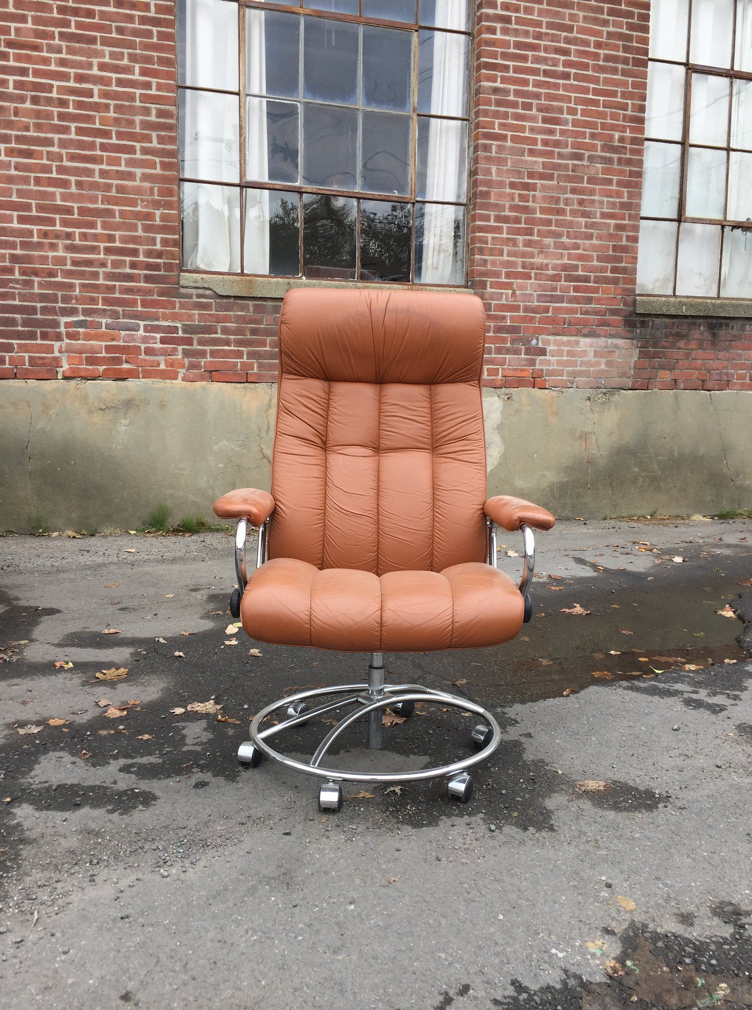 A brown leather office chair is sitting in front of a brick building.