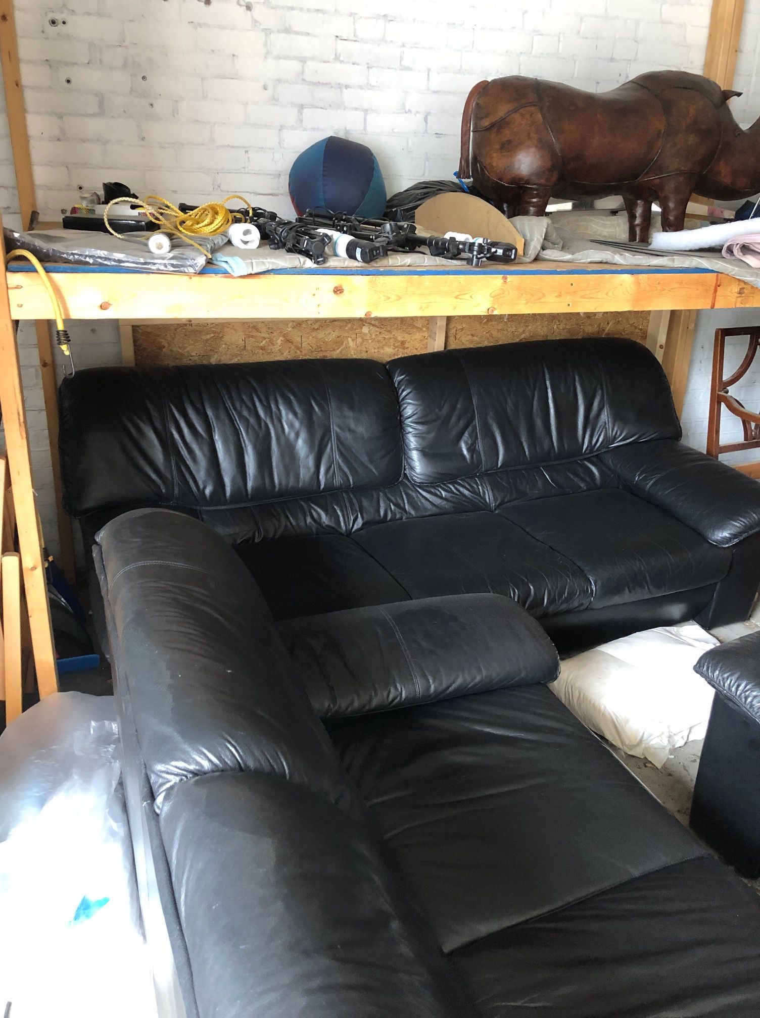 A black leather couch is sitting on top of a wooden shelf in a room.