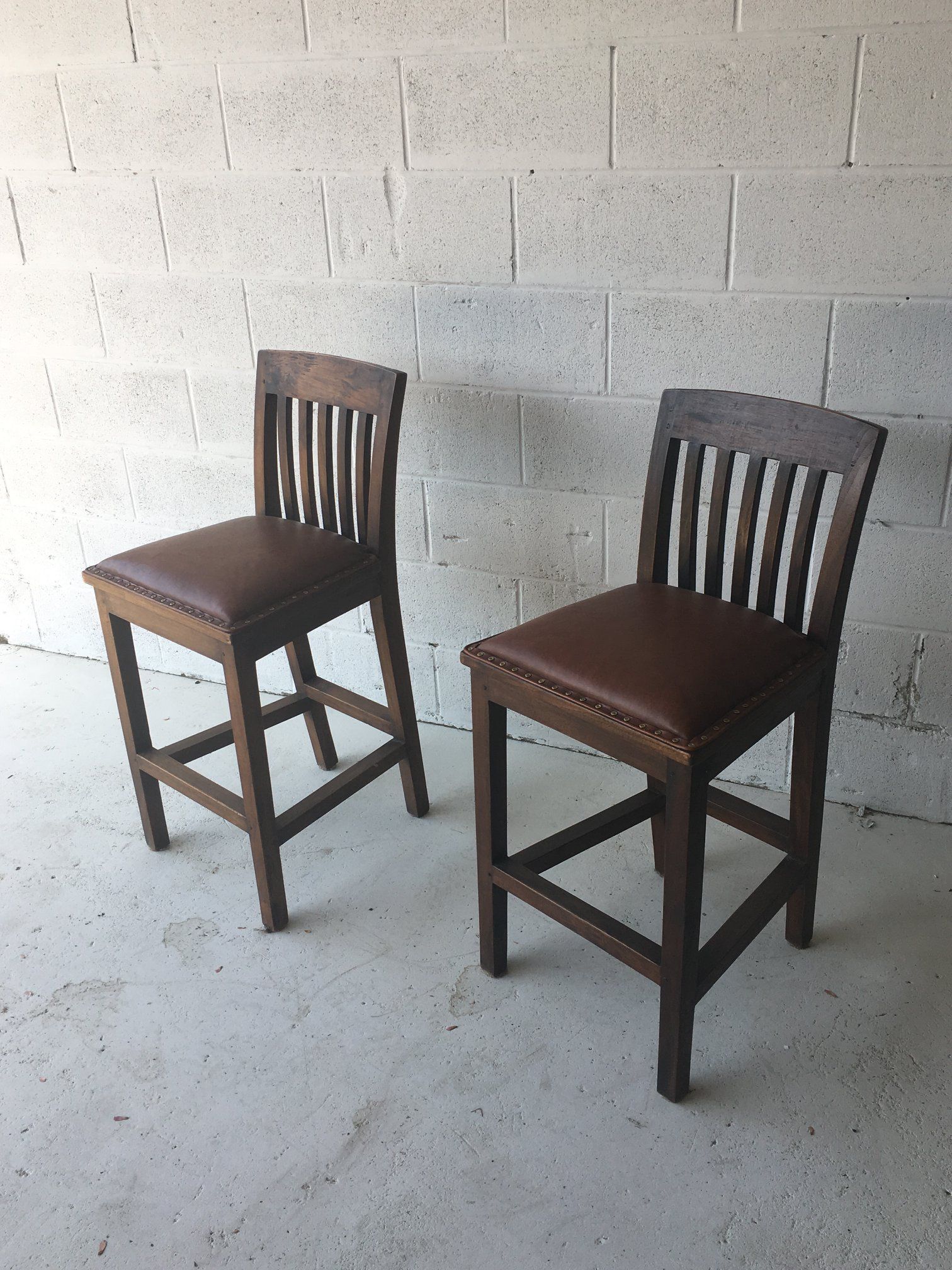 Two wooden bar stools are sitting next to each other in front of a brick wall.