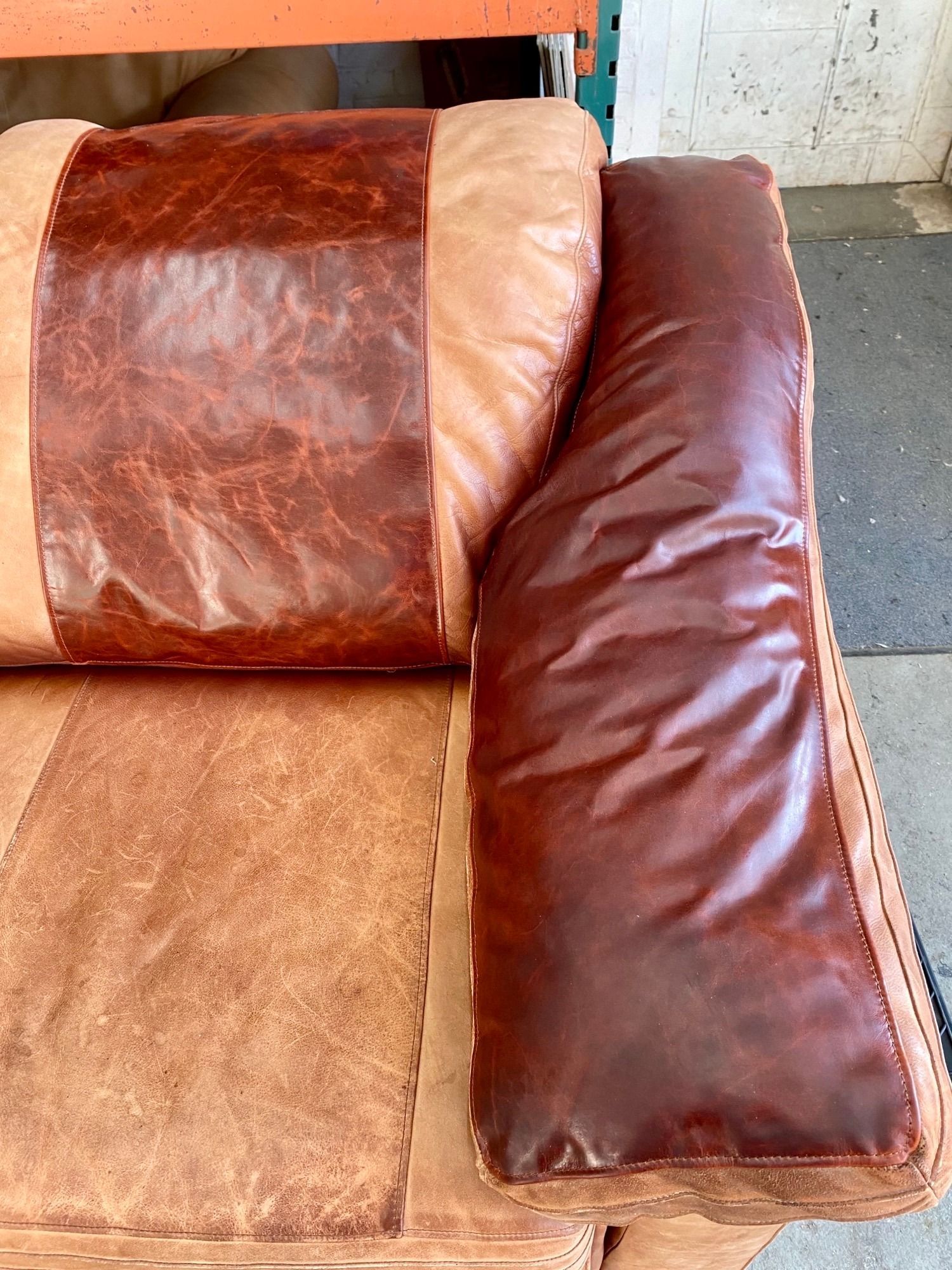 A close up of a brown leather couch with two pillows on it.