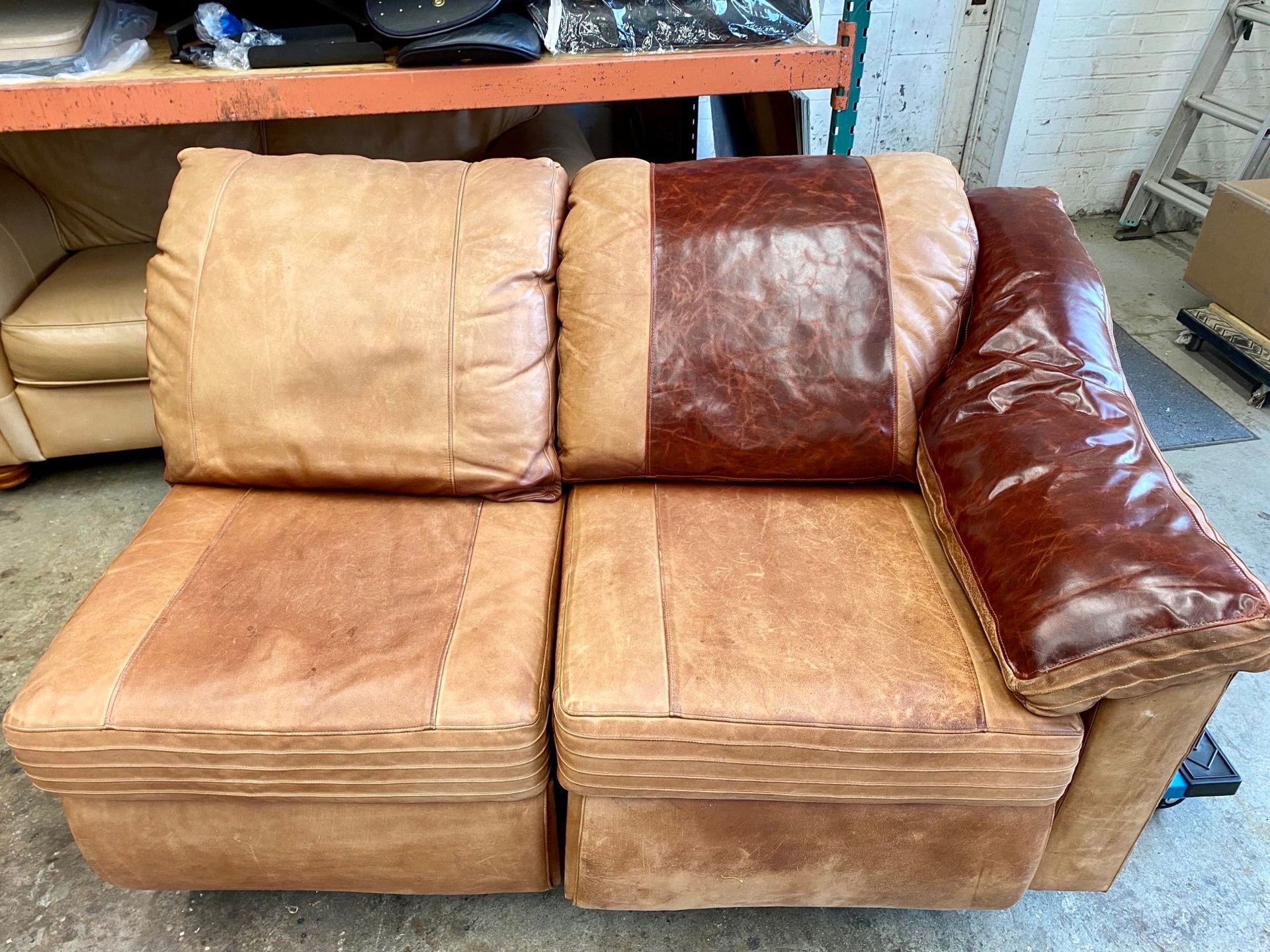 A brown leather couch is sitting in a room next to a shelf.