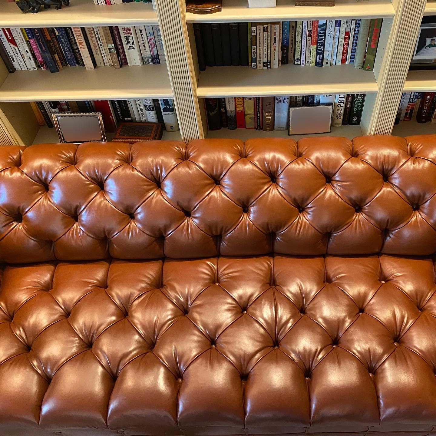 A brown leather couch is sitting in front of a bookshelf filled with books.