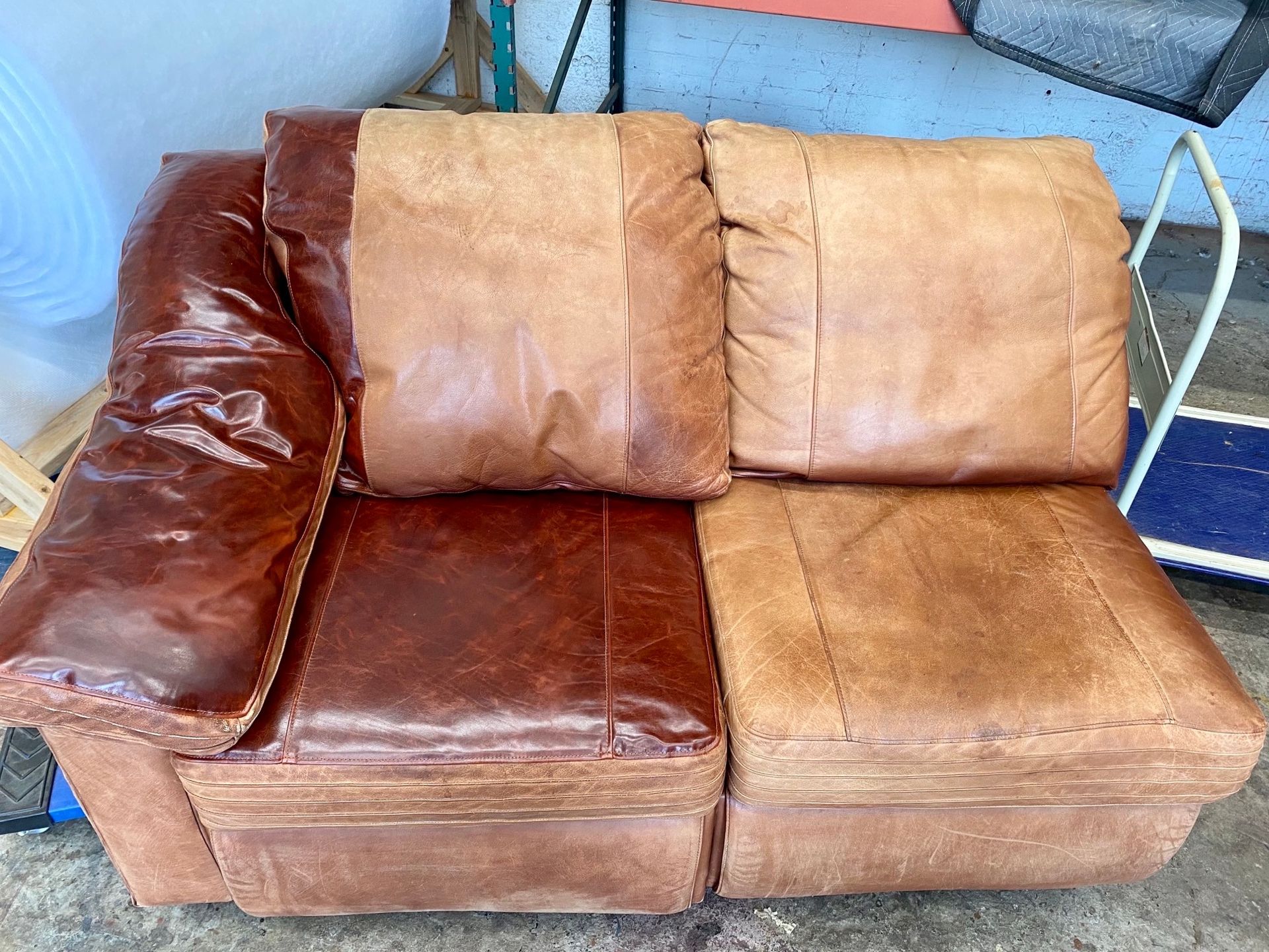 A brown leather couch is sitting in a garage next to a cart.