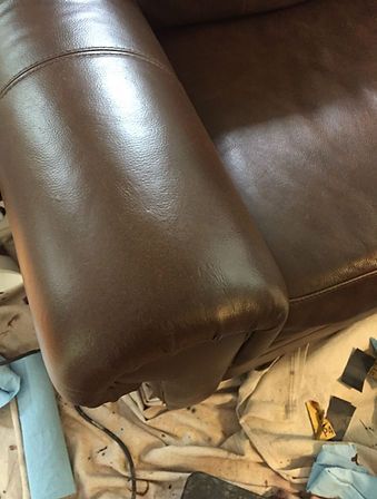 The arm of a brown leather couch is being painted.