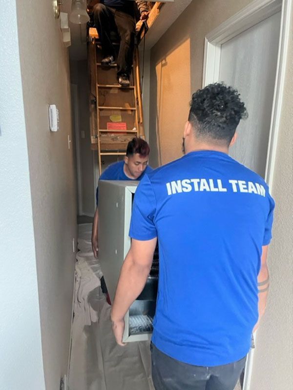 Men in blue shirts carrying an AC unit.