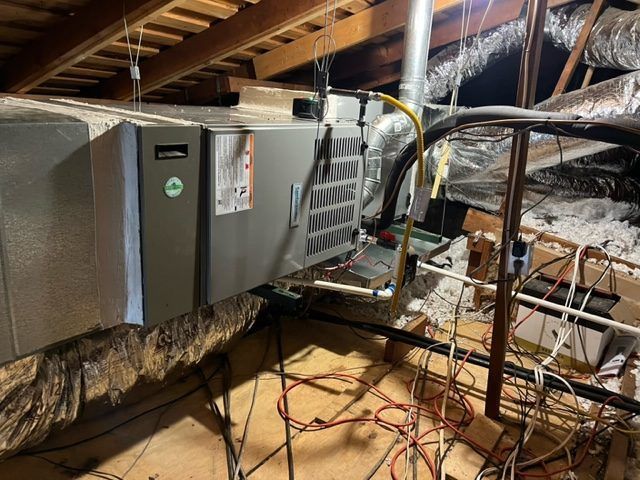 HVAC unit in attic, with exposed wires and ductwork. Gray unit with yellow gas line.