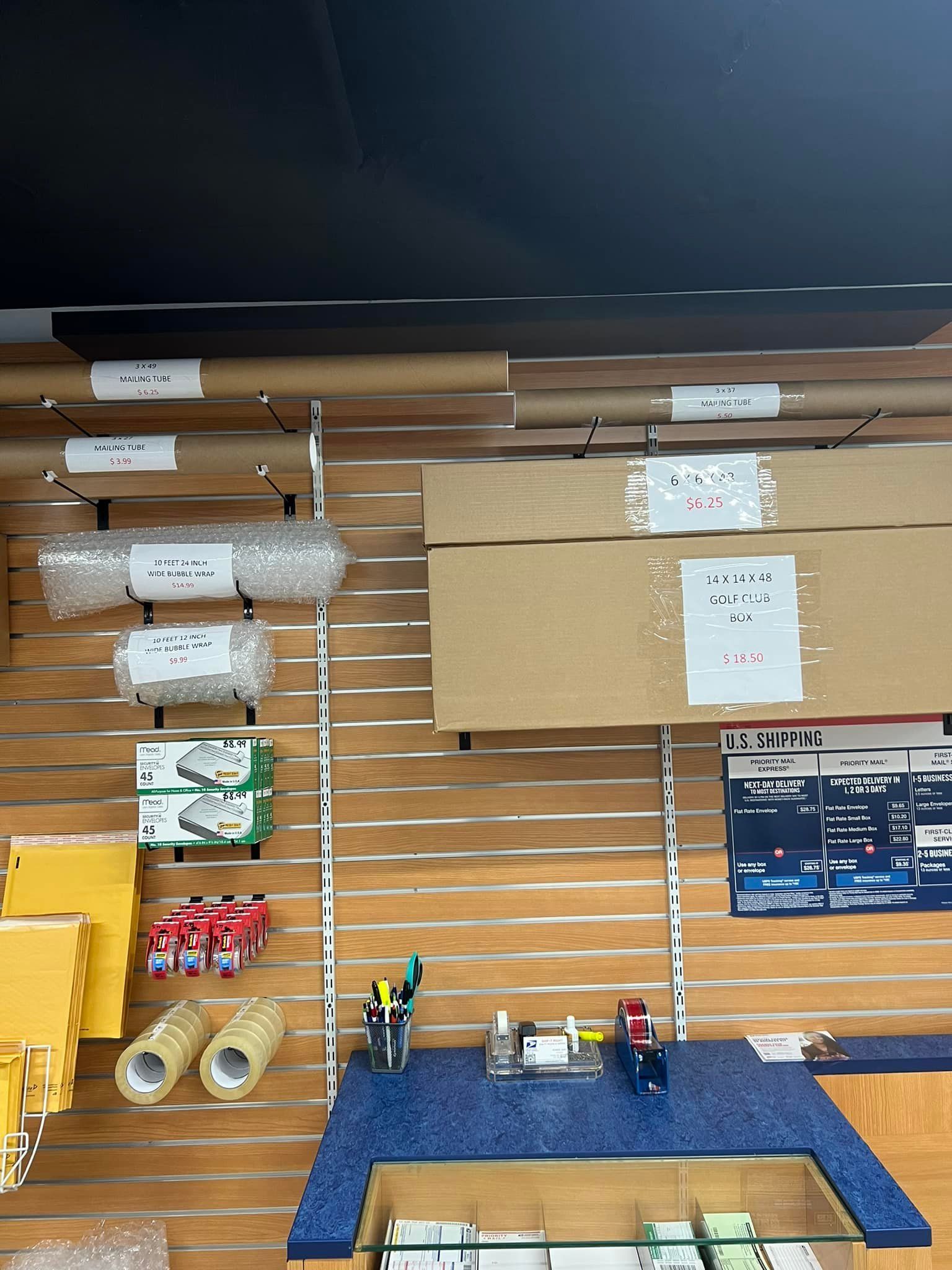 A wall display in a store featuring various shipping supplies like bubble wrap, paper rolls, tape, and boxes on shelving.