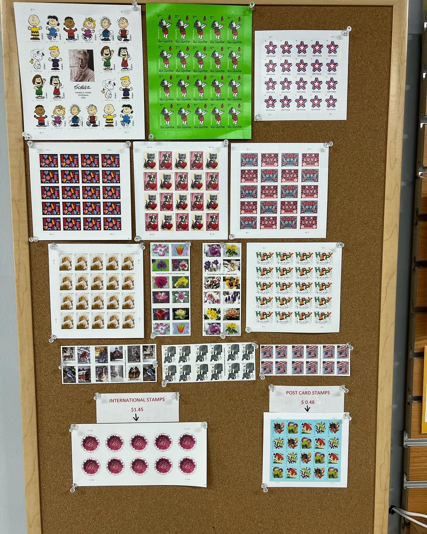 A cork bulletin board displaying various sheets of collectible postage stamps, organized in a grid-like arrangement.