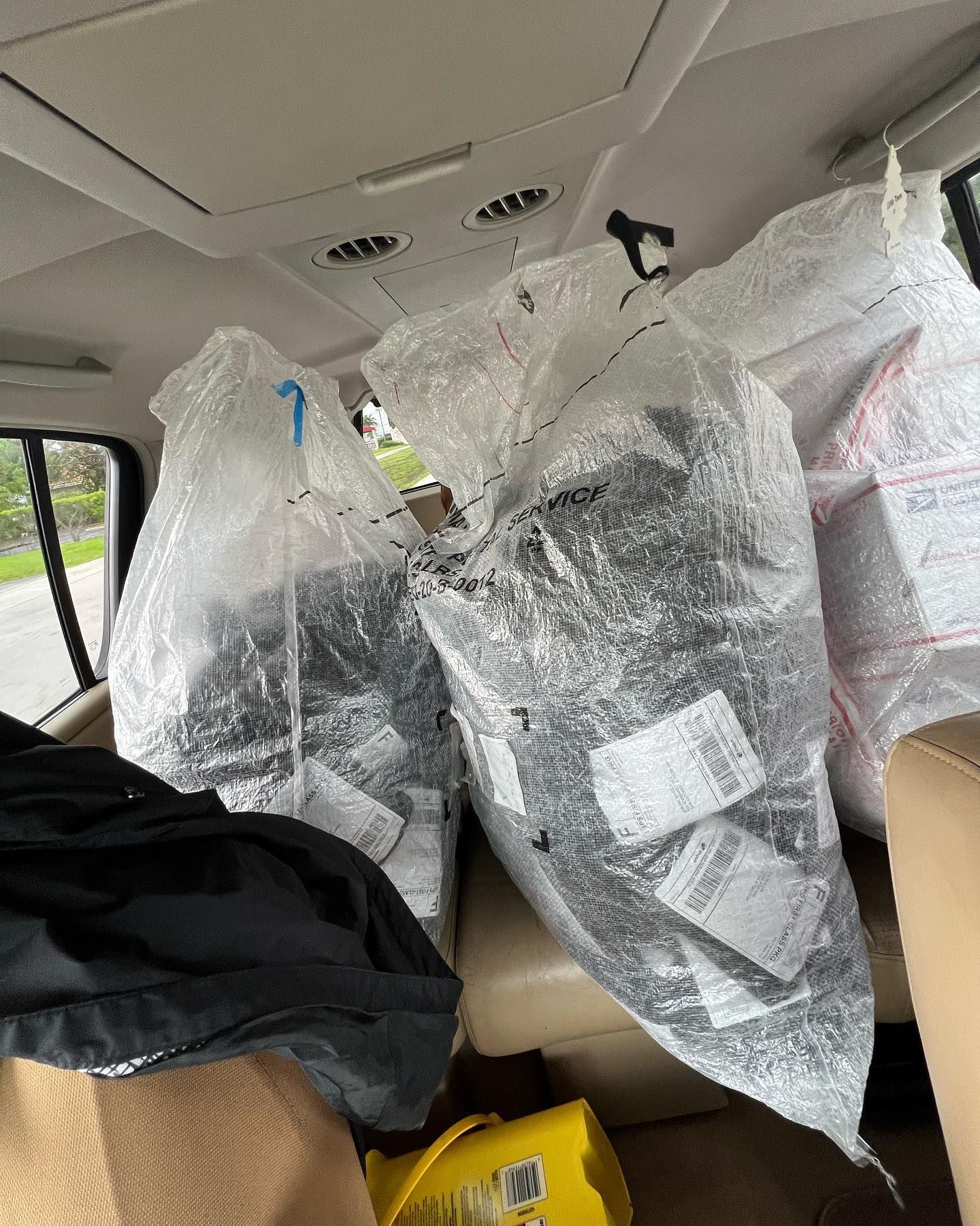 Large clear plastic bags filled with packages are stacked on the back seat of a vehicle.