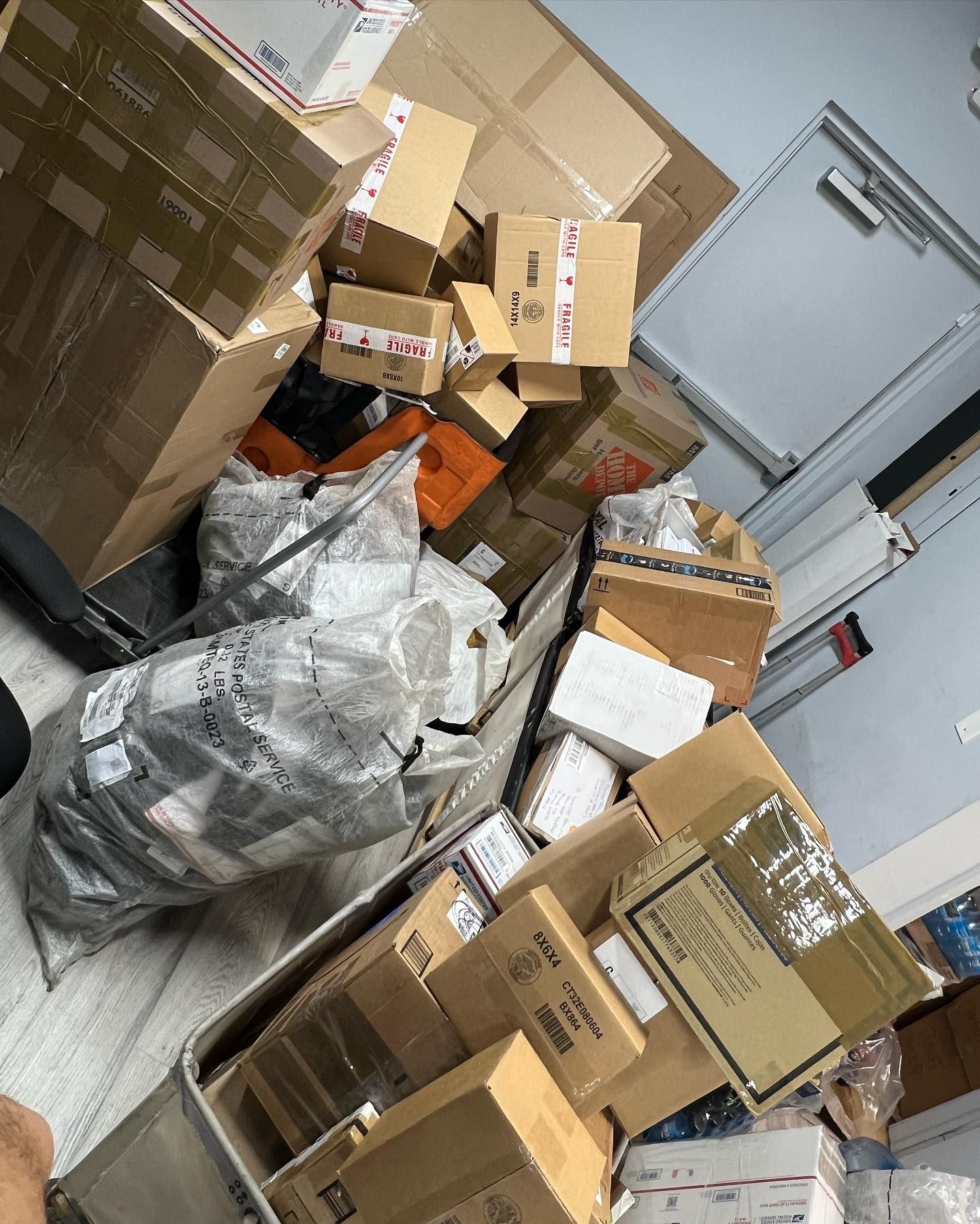 A storage area filled with a large pile of cardboard shipping boxes and plastic-wrapped parcels stacked on the floor.