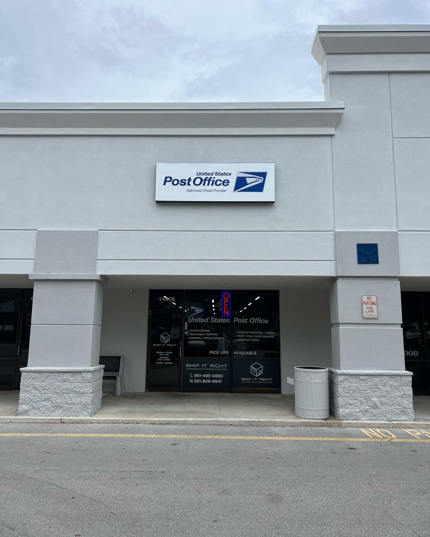 A storefront for a United States Post Office in a strip mall, featuring a white exterior and a sign with the USPS logo.