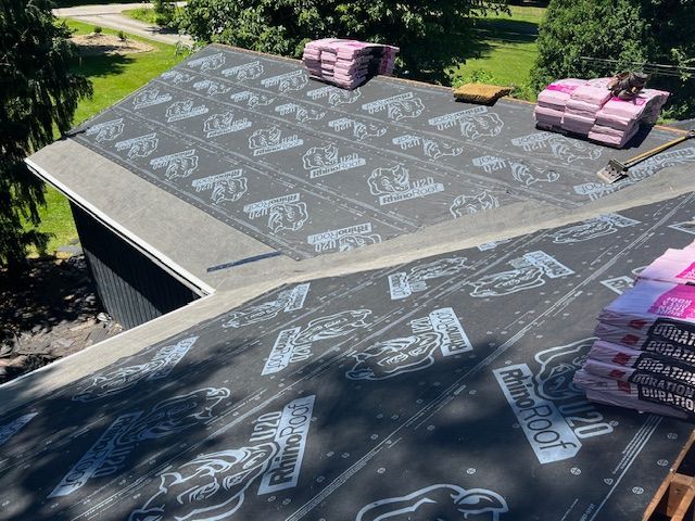 Roof under construction, with new black underlayment and shingles, and stacks of shingles.