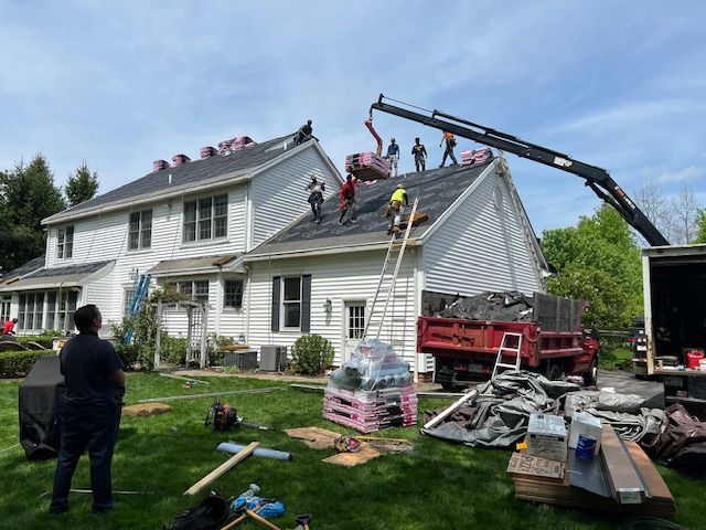 Roofers replacing a shingle roof on a two-story house, crane lifting materials, workers on the roof.