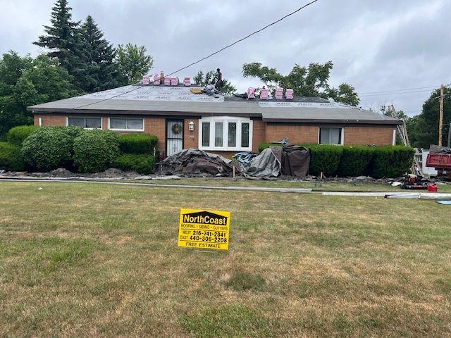 Roofing work in progress on a one-story brick house with green bushes and a North Coast sign in front.