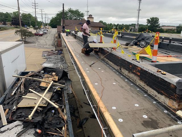 Construction workers on a partially demolished roof, using tools and setting up safety cones.