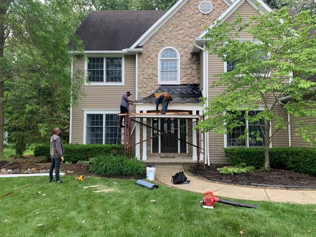 Workers on scaffolding replacing roof over a home's entryway. Two on the roof, one on the ground with a blower.