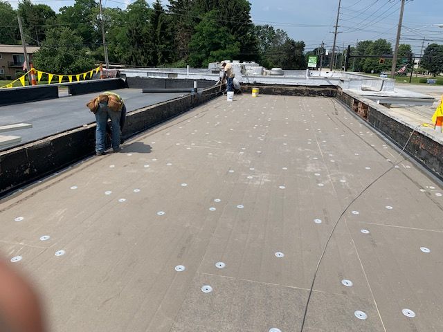 Workers installing roofing on a building. They are placing fasteners on the flat surface.