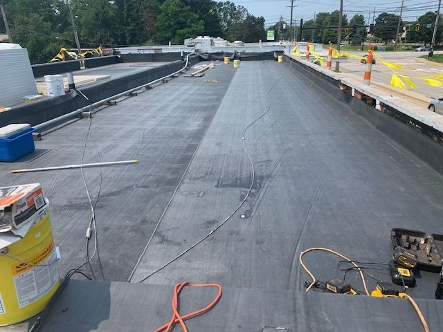 Flat roof under construction with black roofing material, tools, and safety cones.