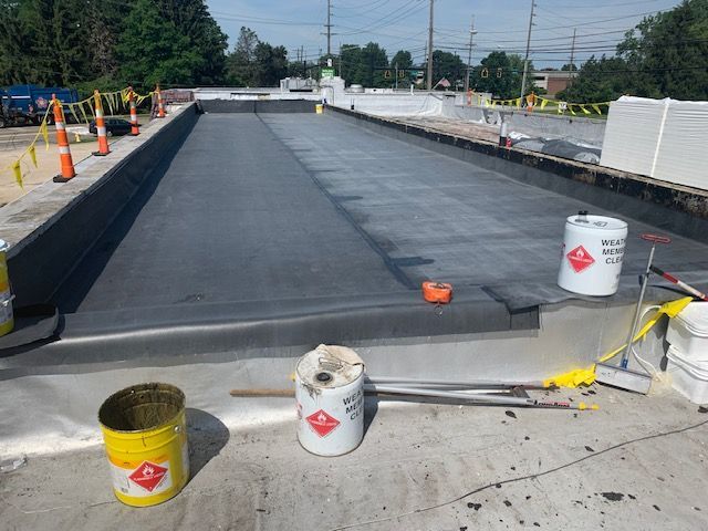 Construction site, flat roof with black waterproofing membrane, tools, and materials.