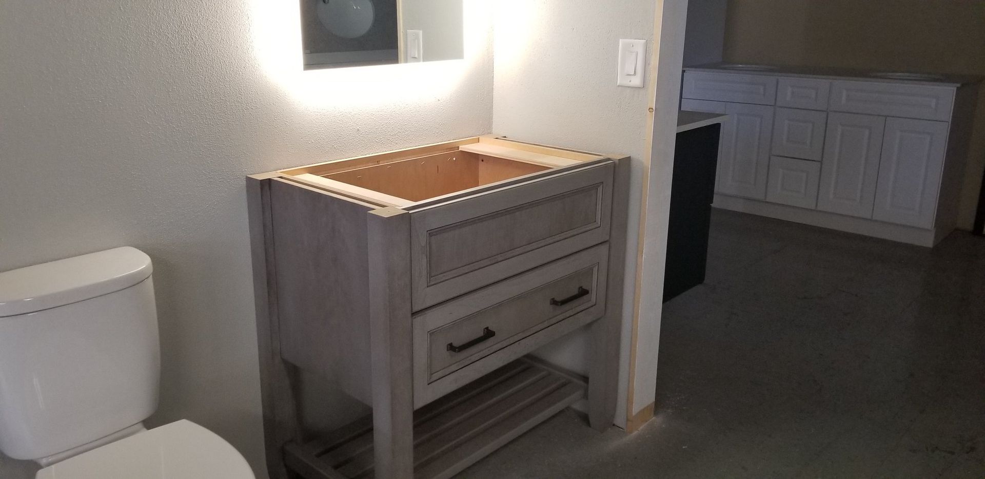 Bathroom with white toilet and unfinished wooden vanity under a lit mirror.