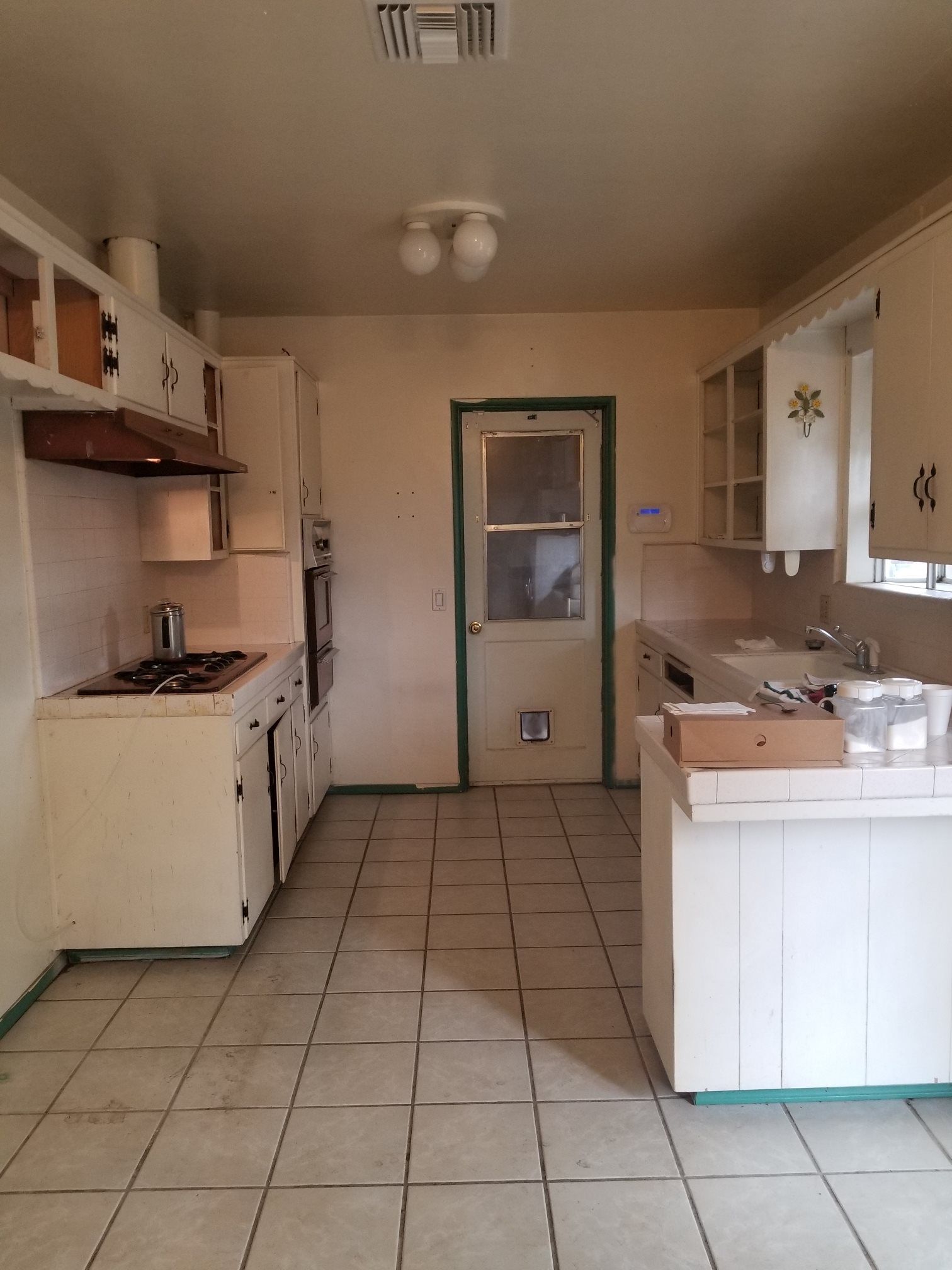 Empty kitchen with off-white cabinets, tiled floor, gas stove, and a back door.