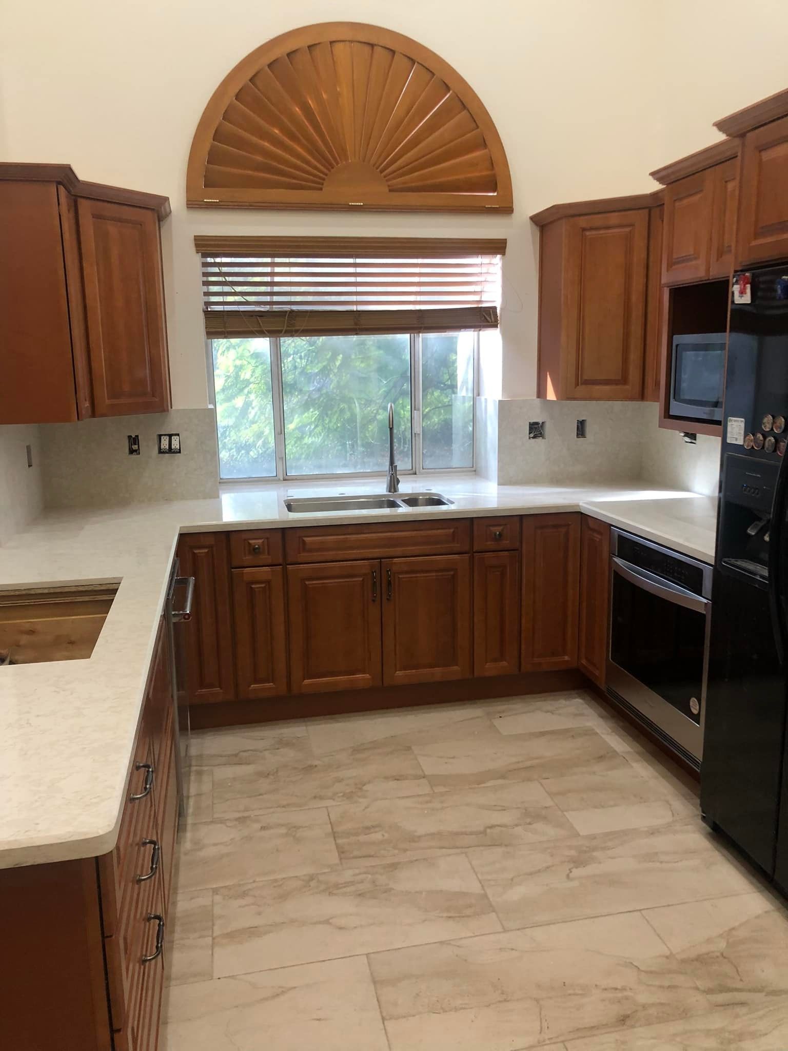 U-shaped kitchen with brown cabinets, light countertops, and large window with wood accents.