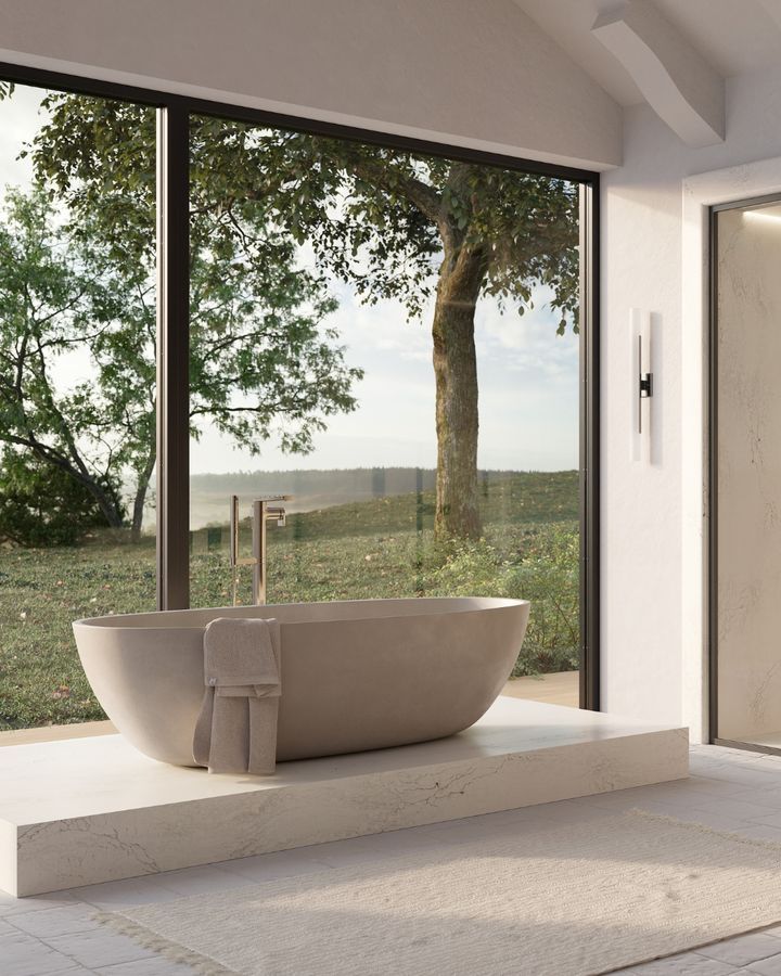 A modern bathroom with a beige soaking tub in front of a large window overlooking a scenic outdoor view.