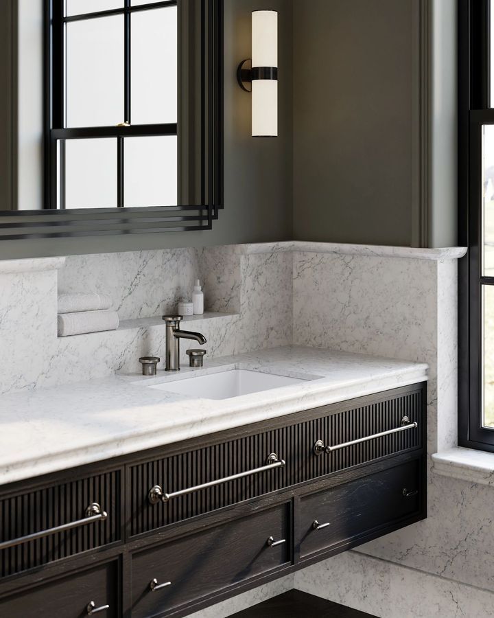 Bathroom with dark cabinetry, white marble countertop and backsplash, and a wall-mounted light.