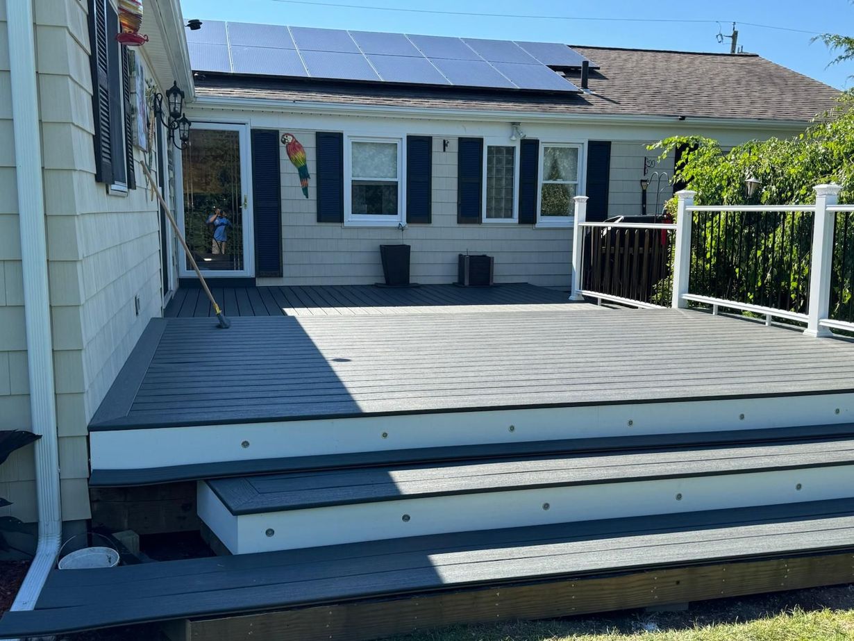 Backyard deck with steps, white railings, and a house with solar panels in bright sunlight
