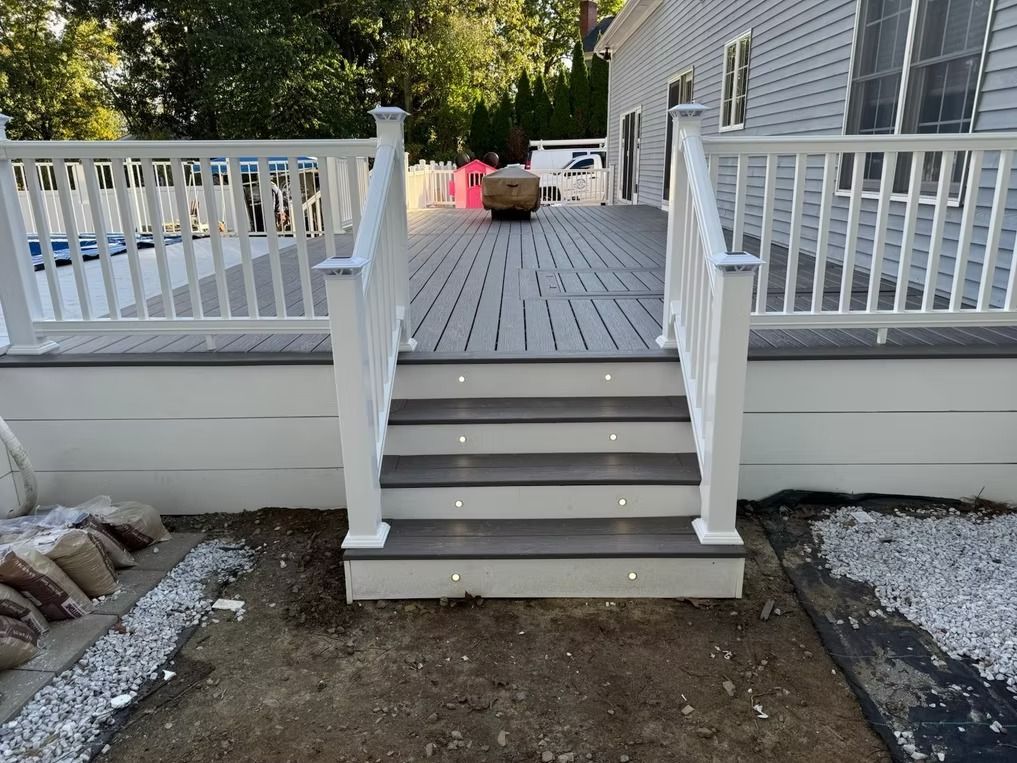 Backyard deck stairs with white railings leading to a raised wooden deck.