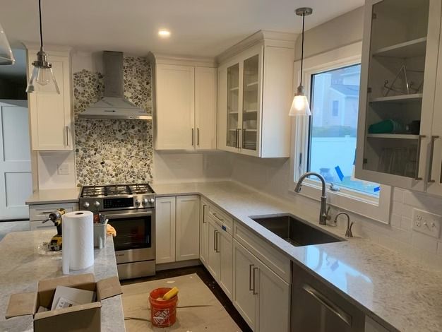 Bright modern kitchen with white cabinets, tiled backsplash, island, and sink under a window