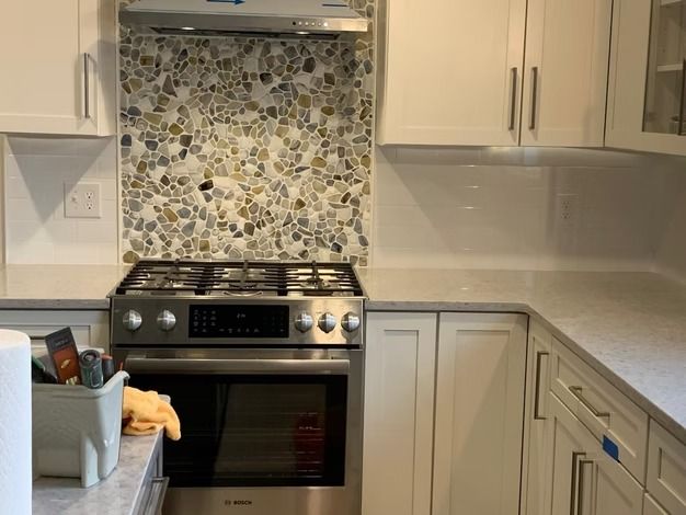Modern kitchen with stainless steel stove, pebble tile backsplash, and light wood cabinets