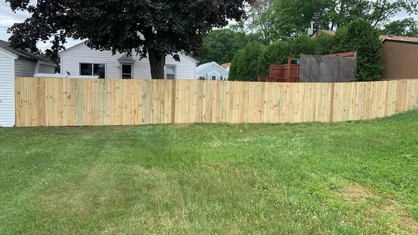 New wooden privacy fence across a grassy backyard with houses and trees behind it