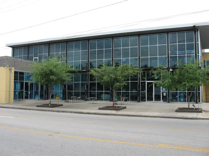 Modern glass-fronted building with trees along the sidewalk beside a quiet street