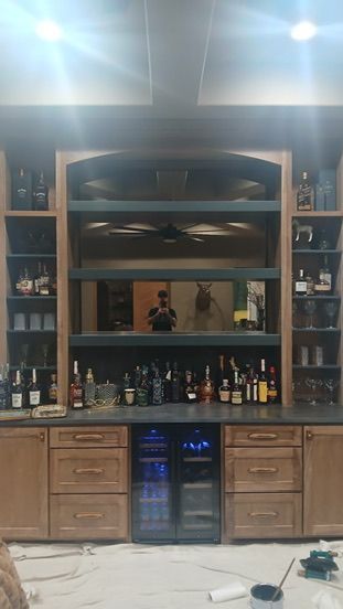 A built-in wood home bar with shelves, a mirror, a wine cooler, and drawers, currently undergoing renovation.