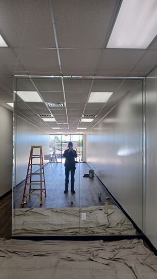 A large mirror installed in an unfinished room reflects a ladder, tools, and a person taking the photo.