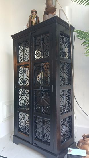 A tall, black wooden cabinet with ornate metal scrollwork panels on its doors, topped with decorative glass vases.