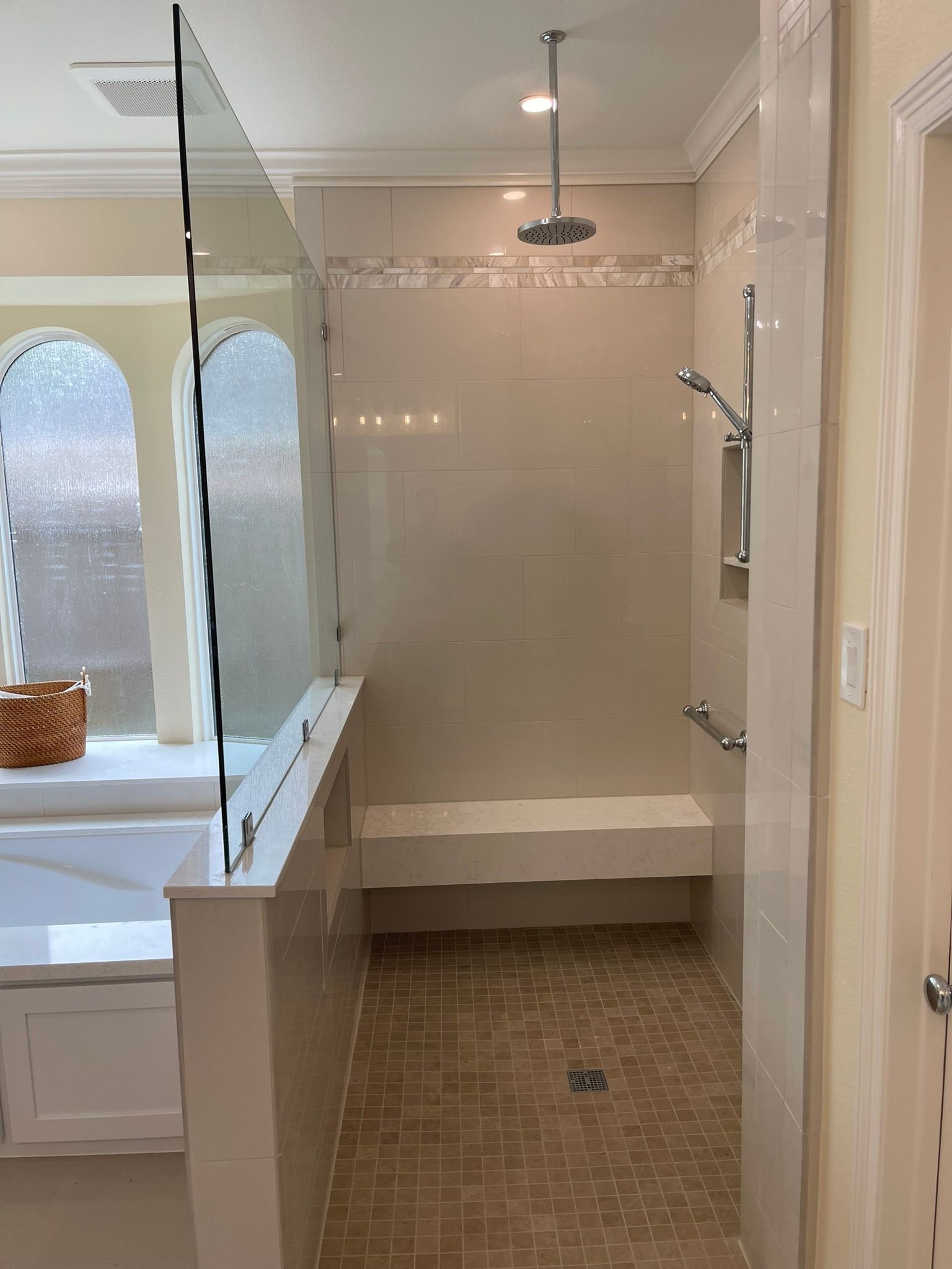 A walk-in shower with beige tile, a built-in bench, a ceiling-mounted rainfall showerhead, and a hand-held sprayer.