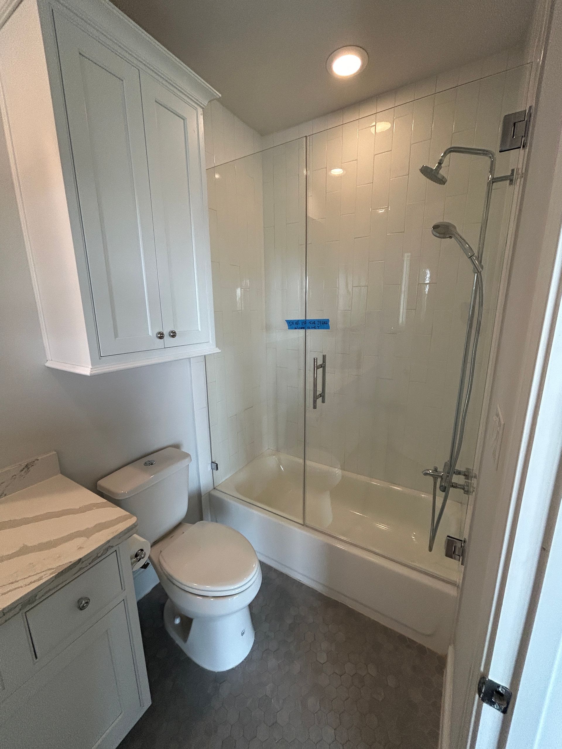 A modern bathroom with a white vanity, toilet, and a glass-enclosed shower featuring chrome fixtures and white tile.