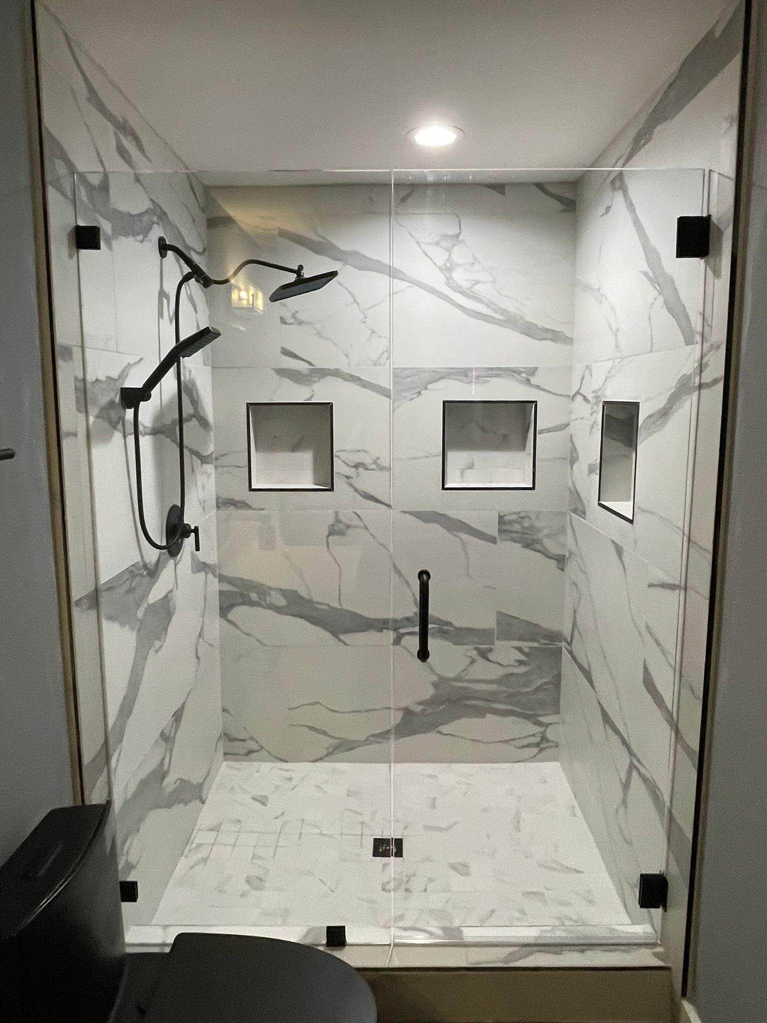 A modern walk-in shower with white and grey marble-patterned tile, glass doors, black hardware, and built-in wall niches.