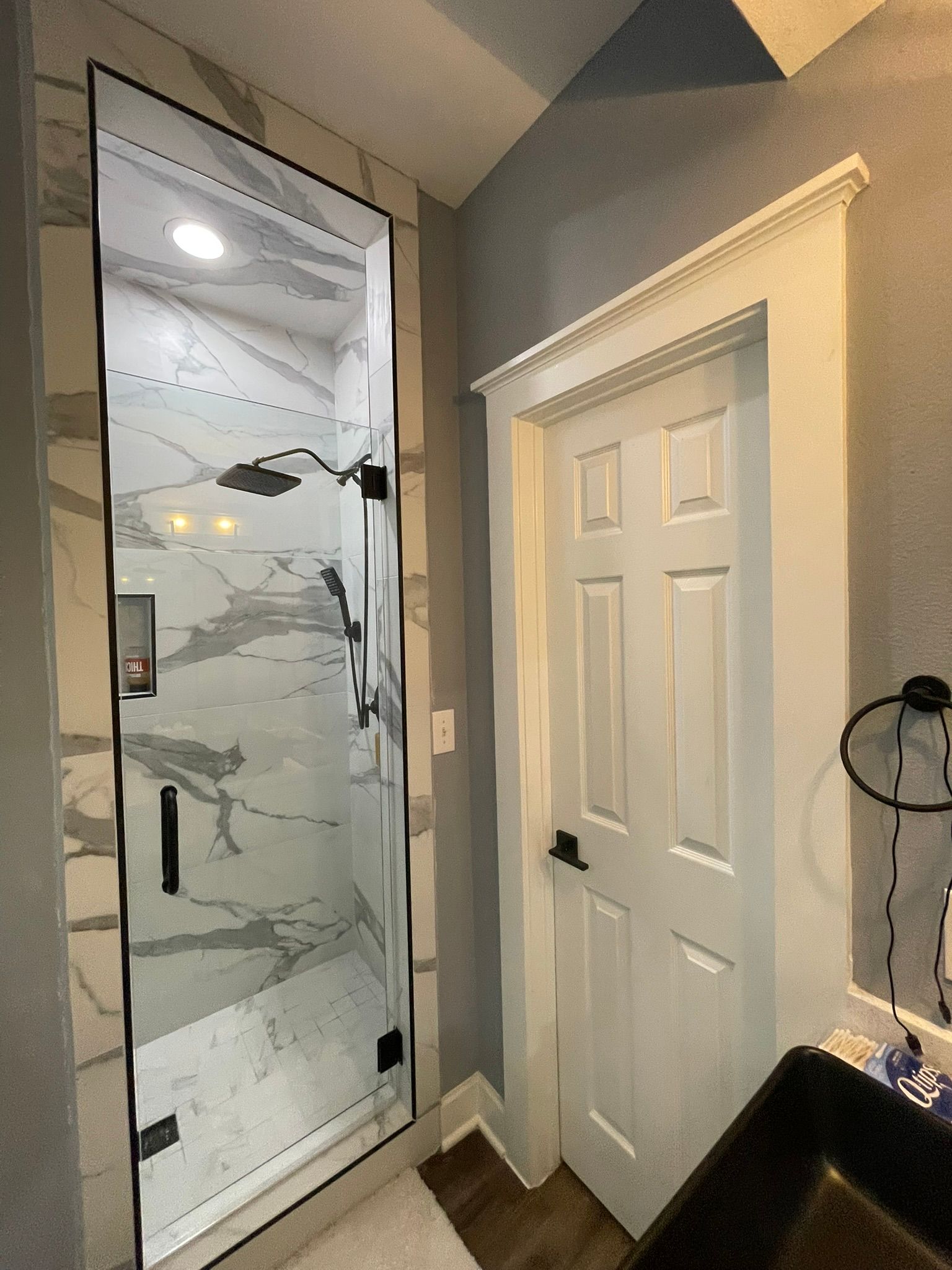 A walk-in shower with white marble tile next to a white six-panel door with molding in a bathroom.