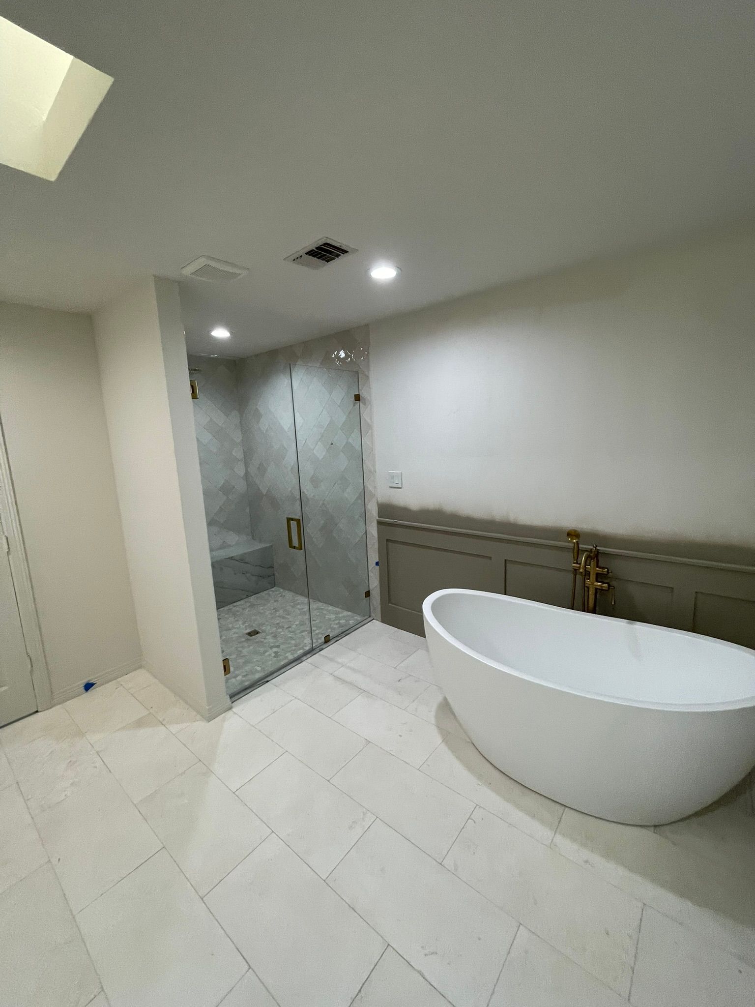 A modern bathroom featuring a white freestanding tub, a large glass-enclosed shower, and light-colored tiled flooring.