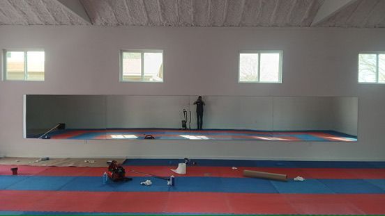 A person standing in front of a large wall mirror in a room with a red and blue foam floor and white walls.