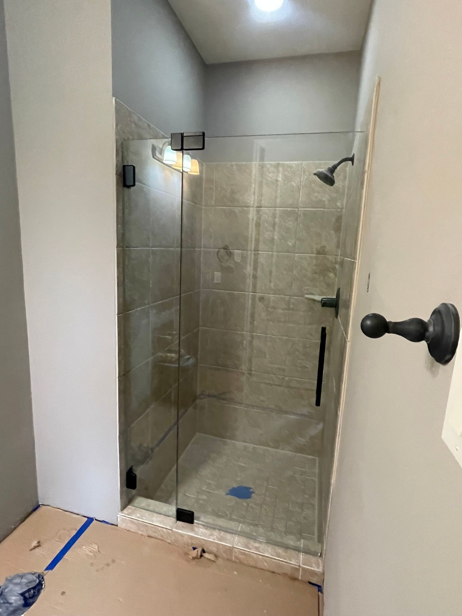 A newly installed glass shower enclosure in a tiled bathroom with protective paper on the floor.