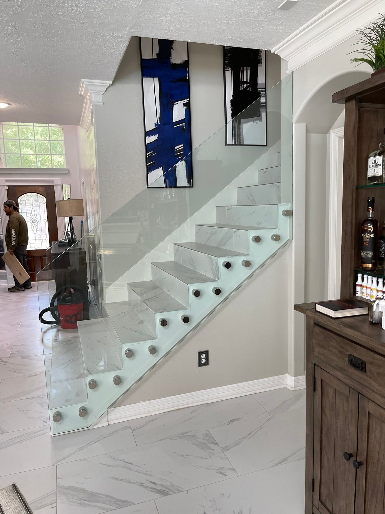 Modern interior with a staircase featuring a clear glass railing attached with metal standoffs, next to two wall art pieces.