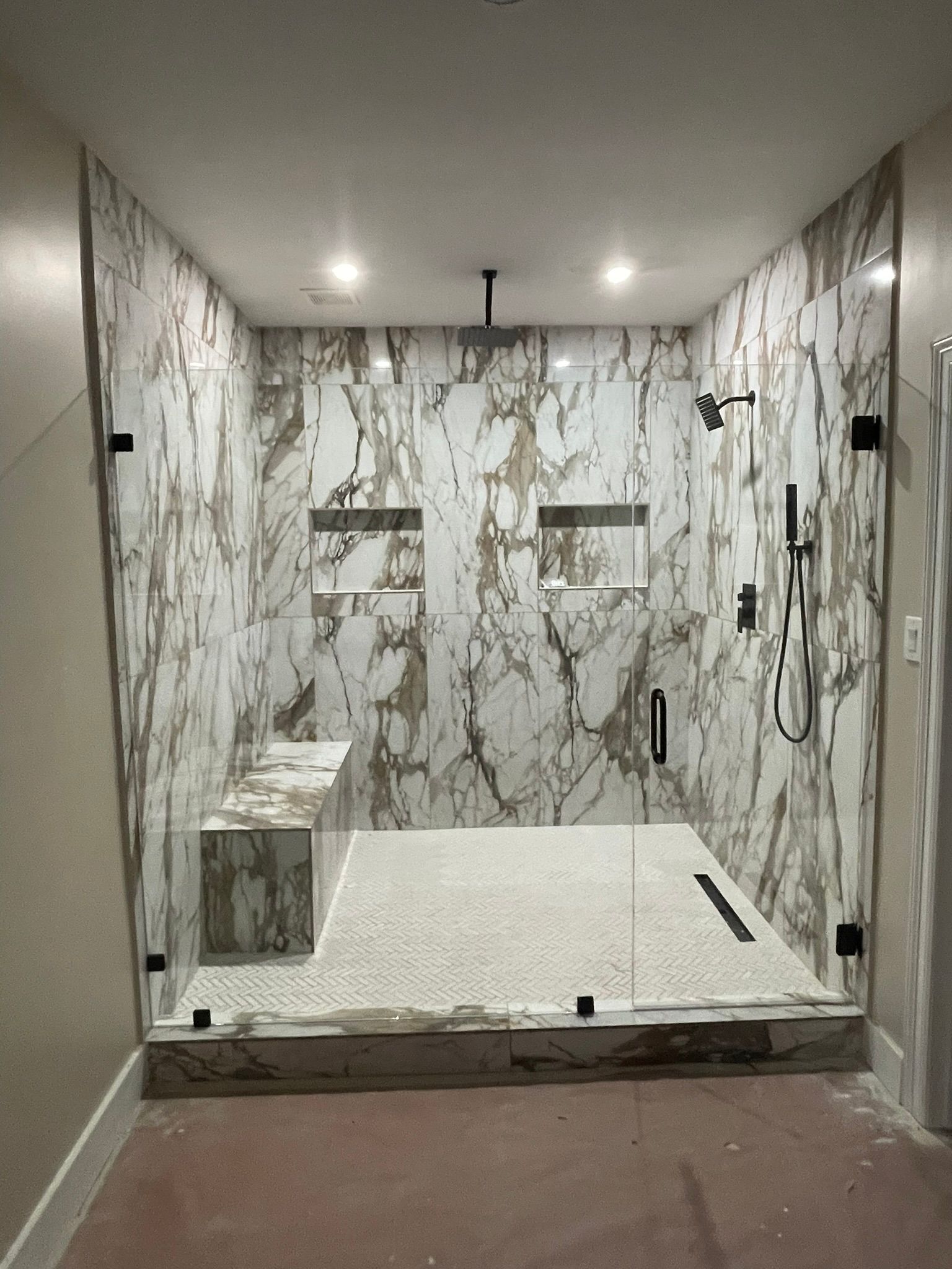 A walk-in shower with white and brown marble-patterned tile, a built-in bench, two niches, and glass doors.