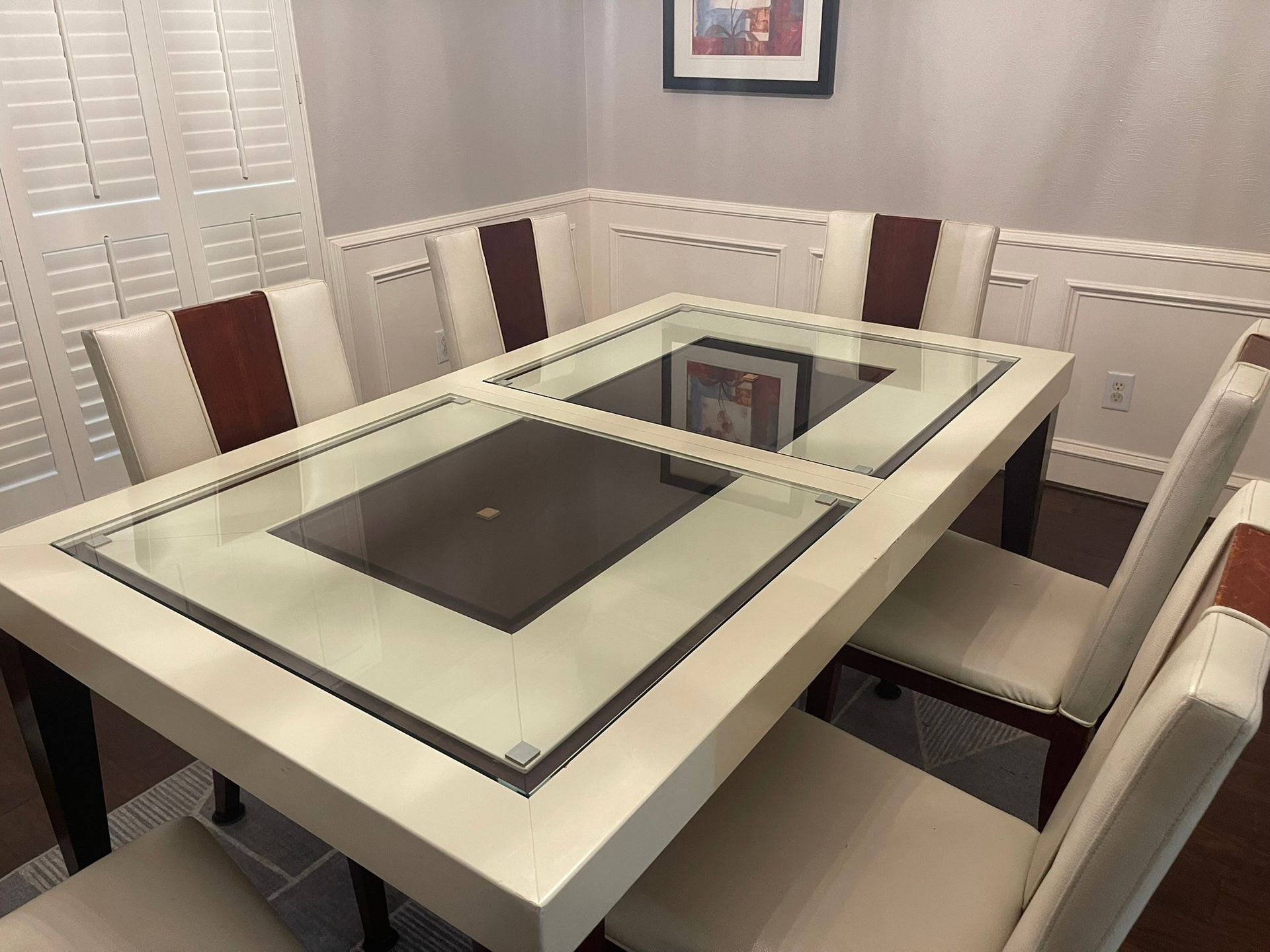 A modern dining table with a cream frame and two-toned glass top, surrounded by six chairs with cream and brown upholstery.