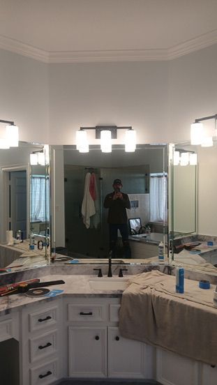 A bathroom vanity with white cabinets, a marble countertop, large angled mirrors, and three modern light fixtures.