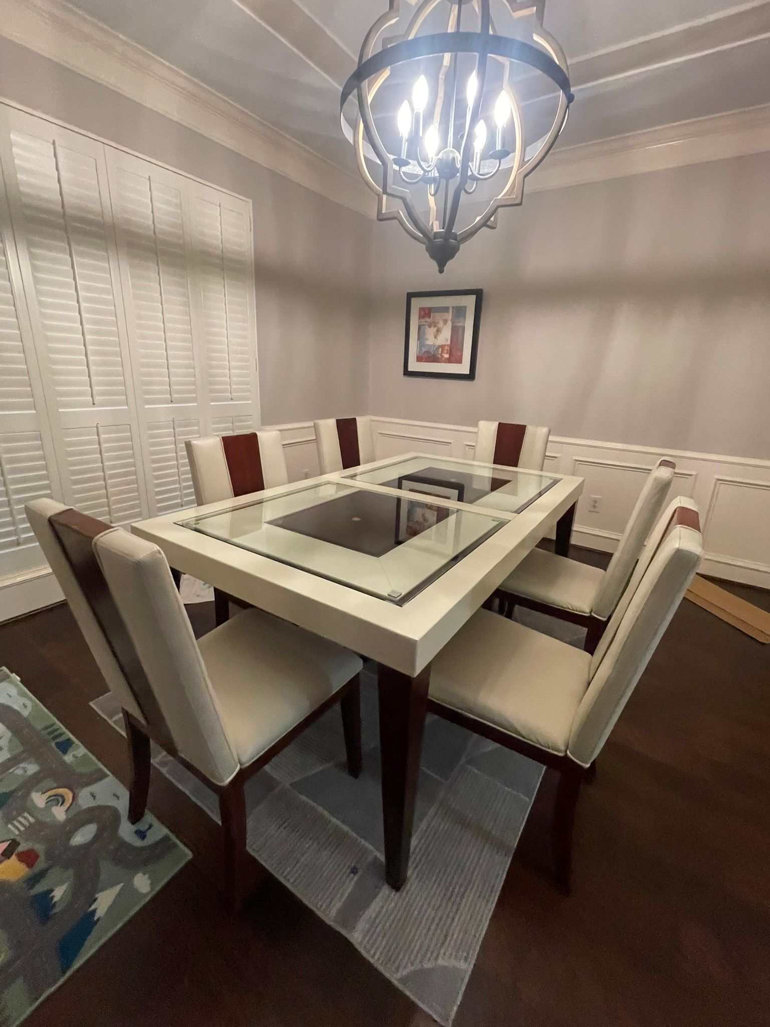 Dining room with a cream-colored table, four chairs with brown accents, a corner bench, and a large metal chandelier.