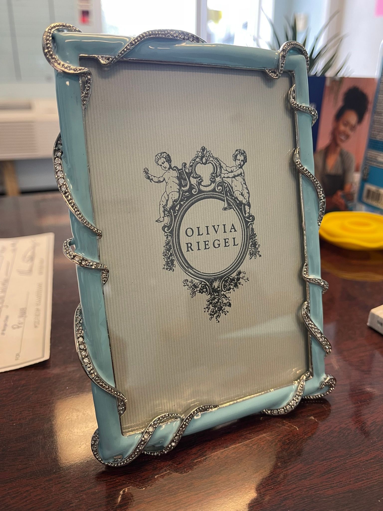 A light blue picture frame with silver vine-like filigree trim resting on a wooden desk.